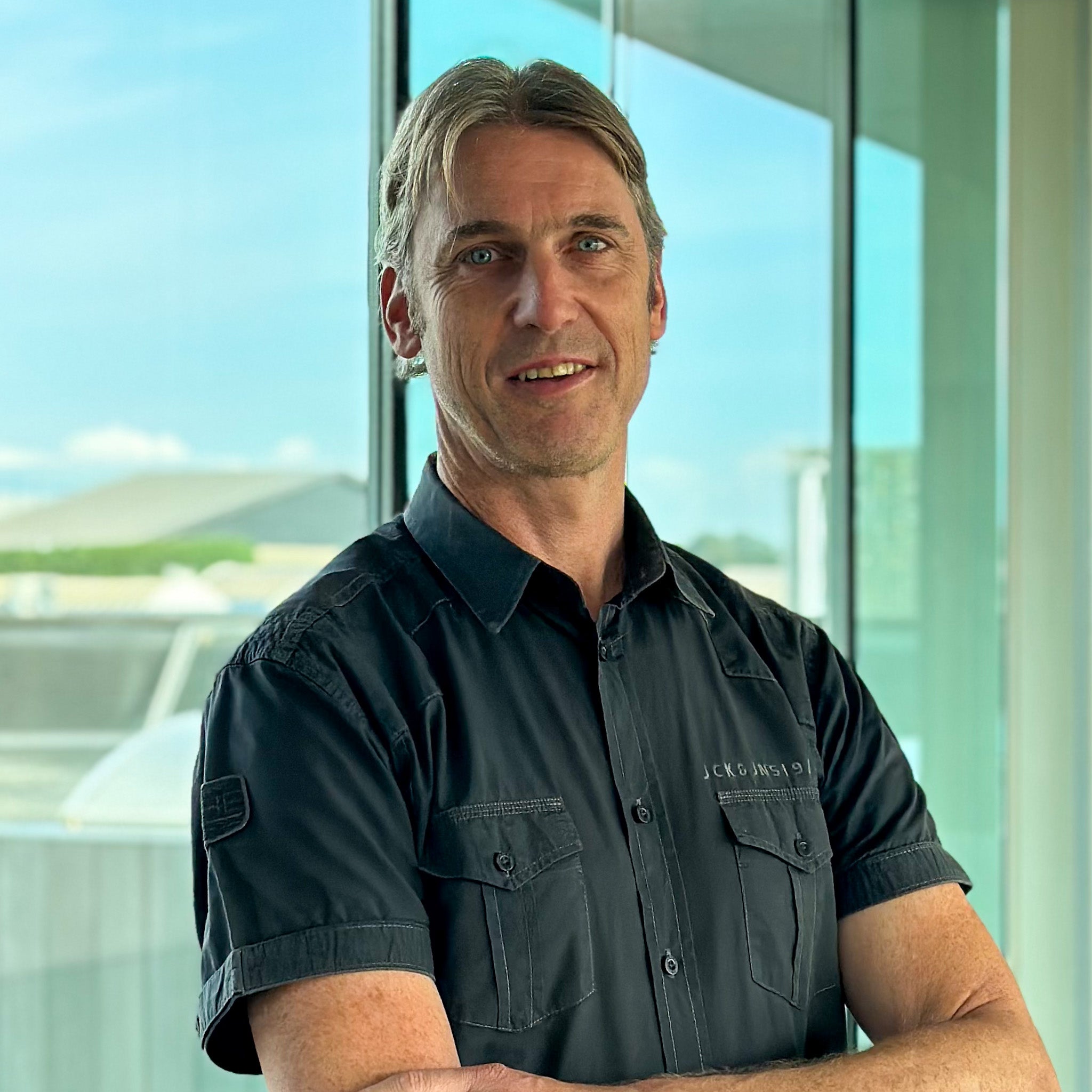 Davy Tytgat, a smiling man with graying hair, wearing a dark short-sleeved shirt, arms crossed.