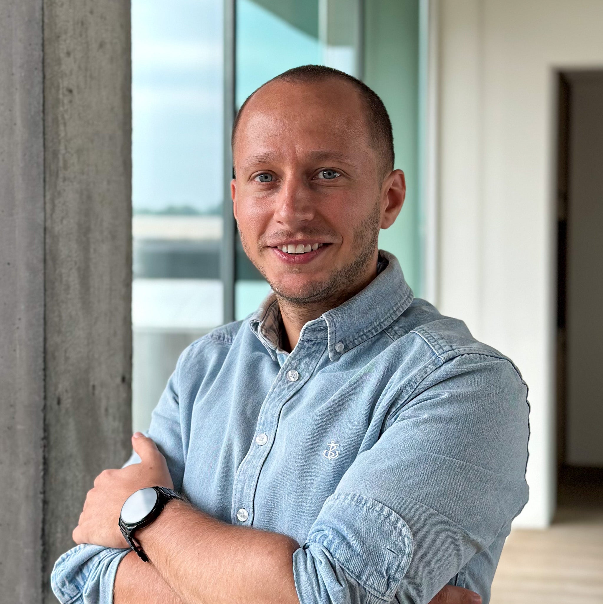 Thijs Declercq, a man with short hair and blue eyes, smiling in a light blue denim shirt with arms crossed.